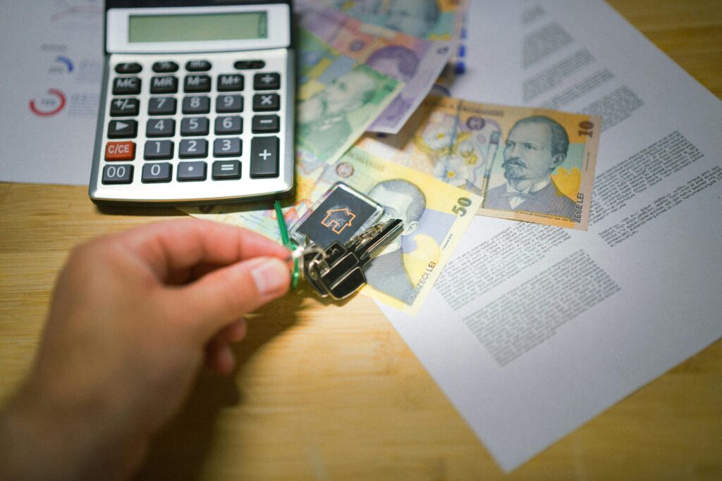 A hand holds keys next to Romanian currency, a calculator, and documents, symbolizing real estate transactions.